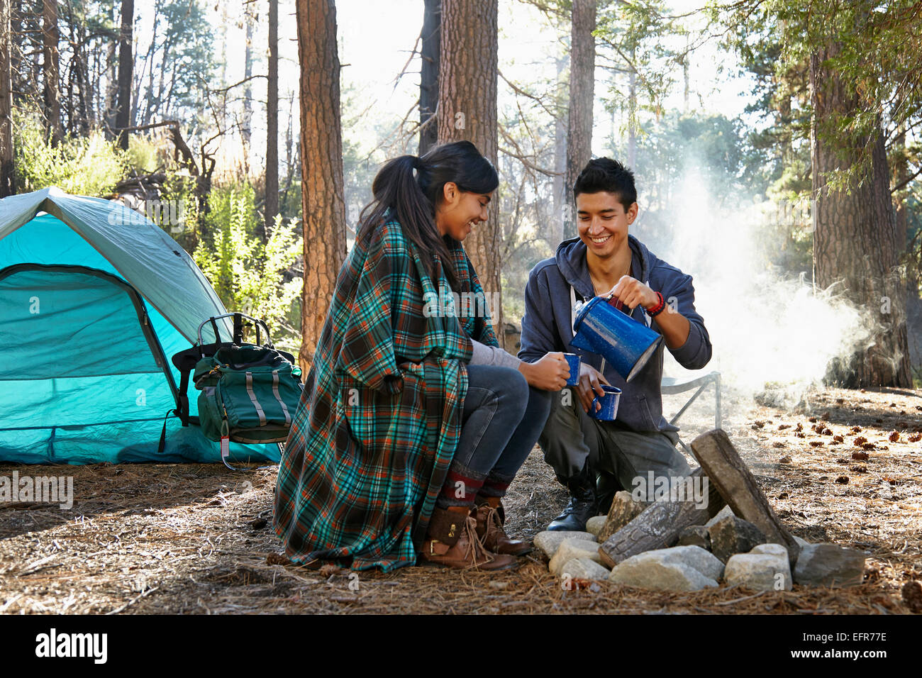 Junges Paar gießt Kaffee am Lagerfeuer im Wald, Los Angeles, Kalifornien, USA Stockfoto
