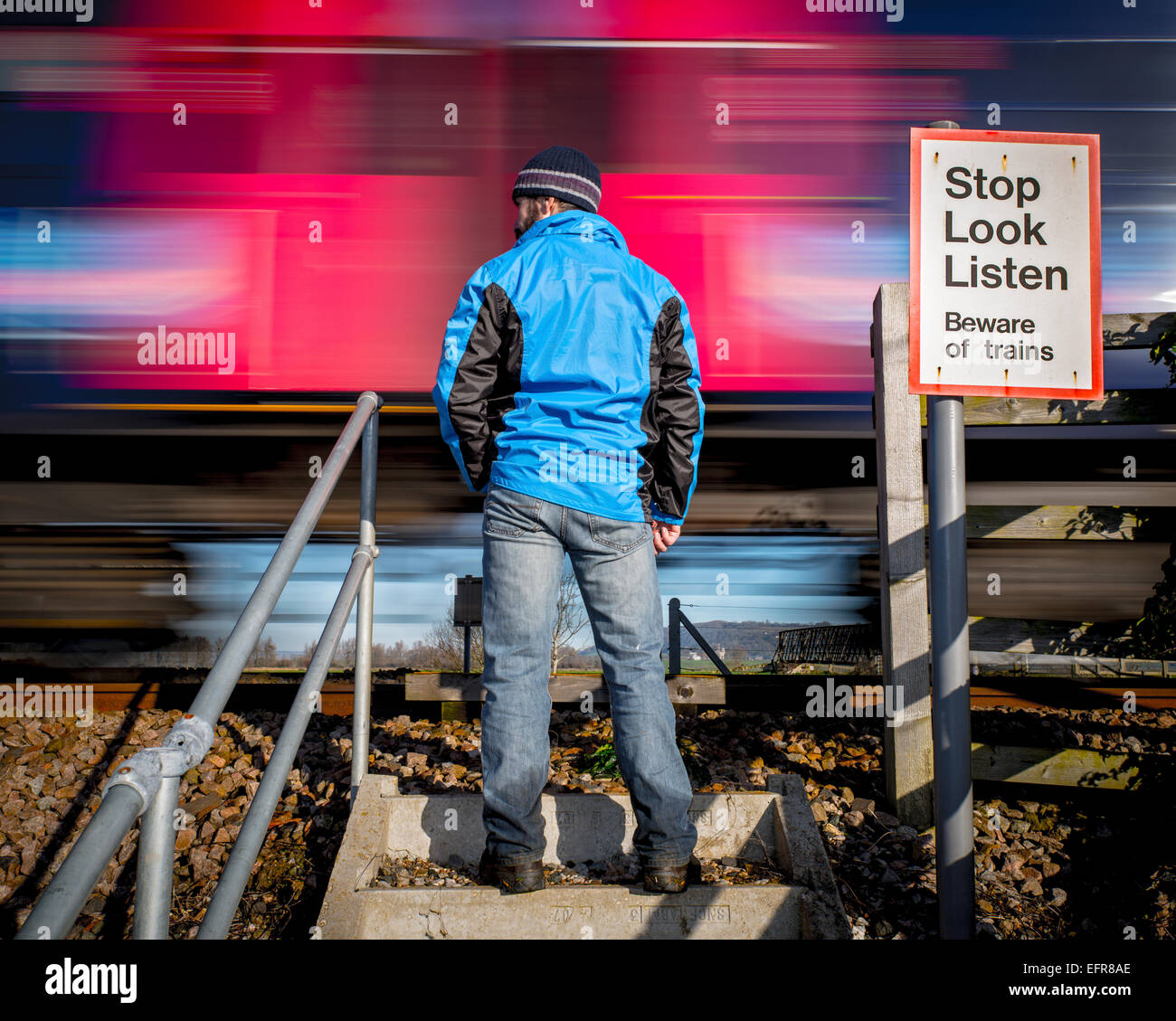 Mann steht auf ländlichen Bahnübergang als Zug vorbei an Geschwindigkeiten Stockfoto
