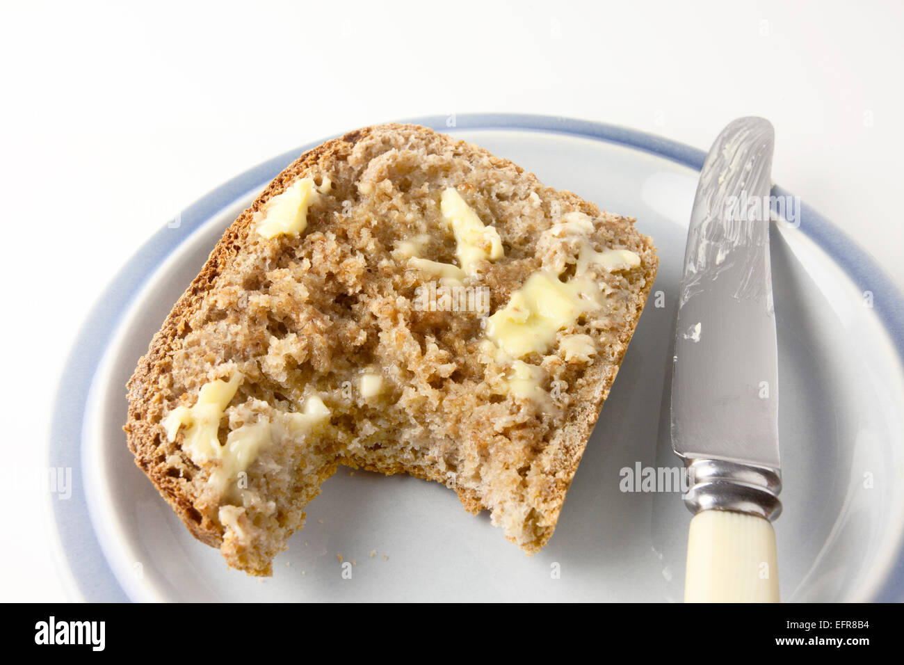 Scheibe des frisch gebackenen warmen Vollkornbrot mit Butter mit Biss genommen auf einem Teller mit einem Messer Stockfoto