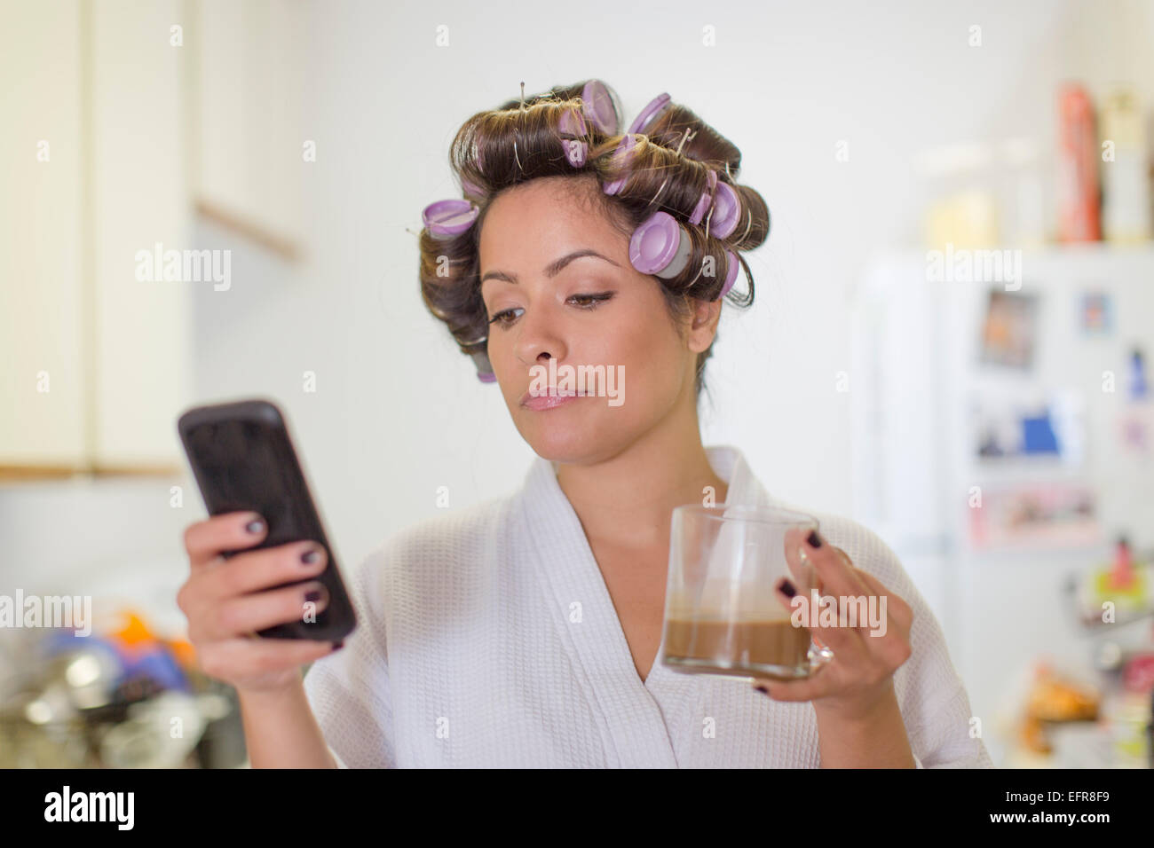 Mitte Erwachsene Frau trägt Lockenwickler und Lesen von SMS-Nachricht auf smartphone Stockfoto