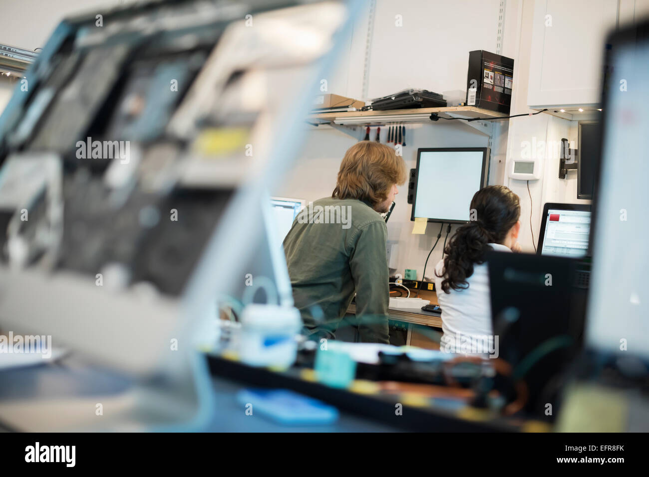 Computer-Werkstatt. Zwei Personen sitzen mit Bildschirmen und Computermonitoren in verschiedenen Stadien der Reparatur. Stockfoto