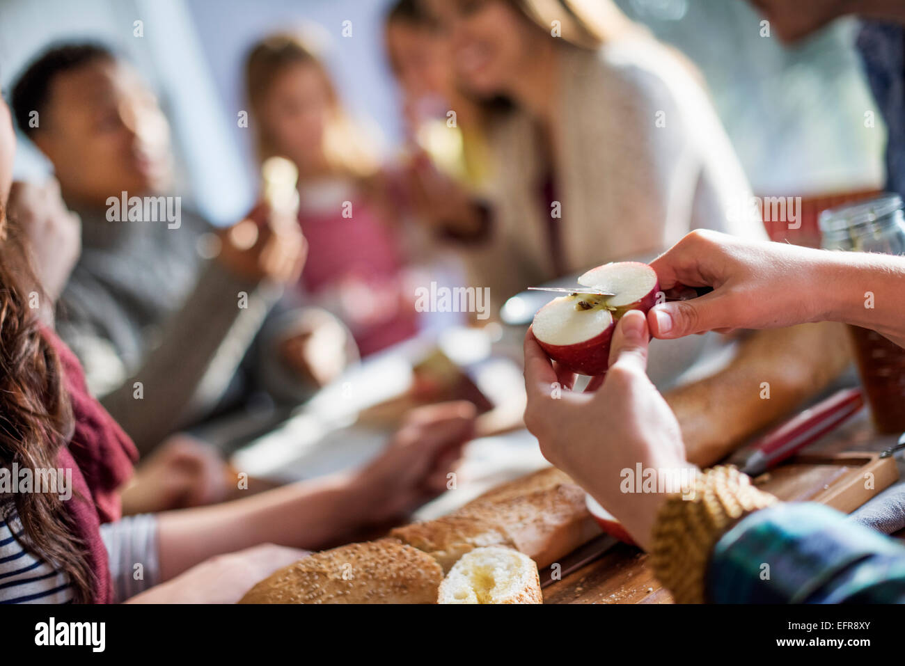 Eine Gruppe von Menschen an einem Tisch sitzen, Essen und plaudern. Eine Frau, schneiden einen Apfel. Stockfoto