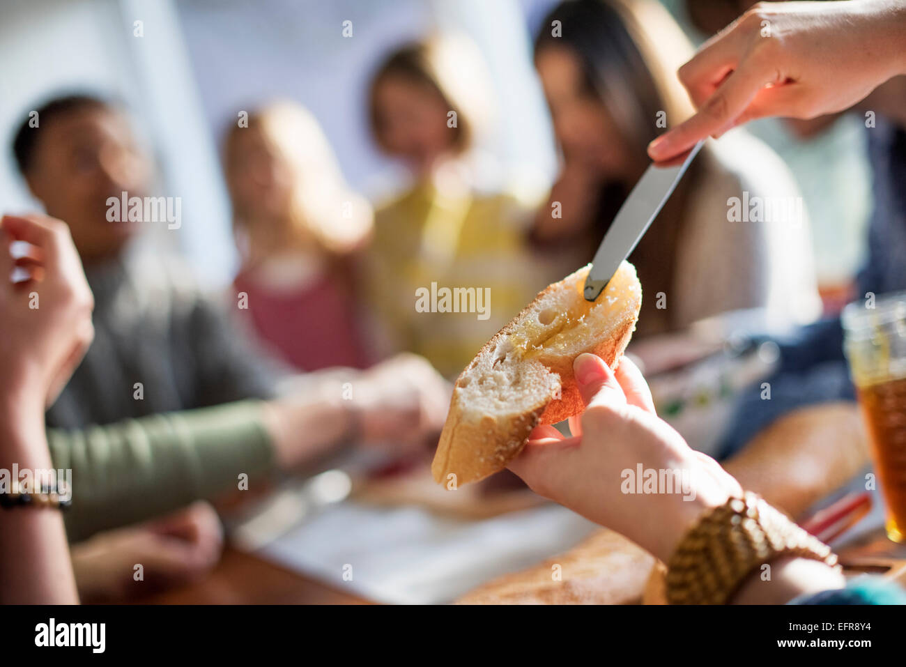 Eine Gruppe von Menschen an einem Tisch sitzen, Essen und plaudern. Eine Frau, ein Stück Baguette schmieren. Stockfoto