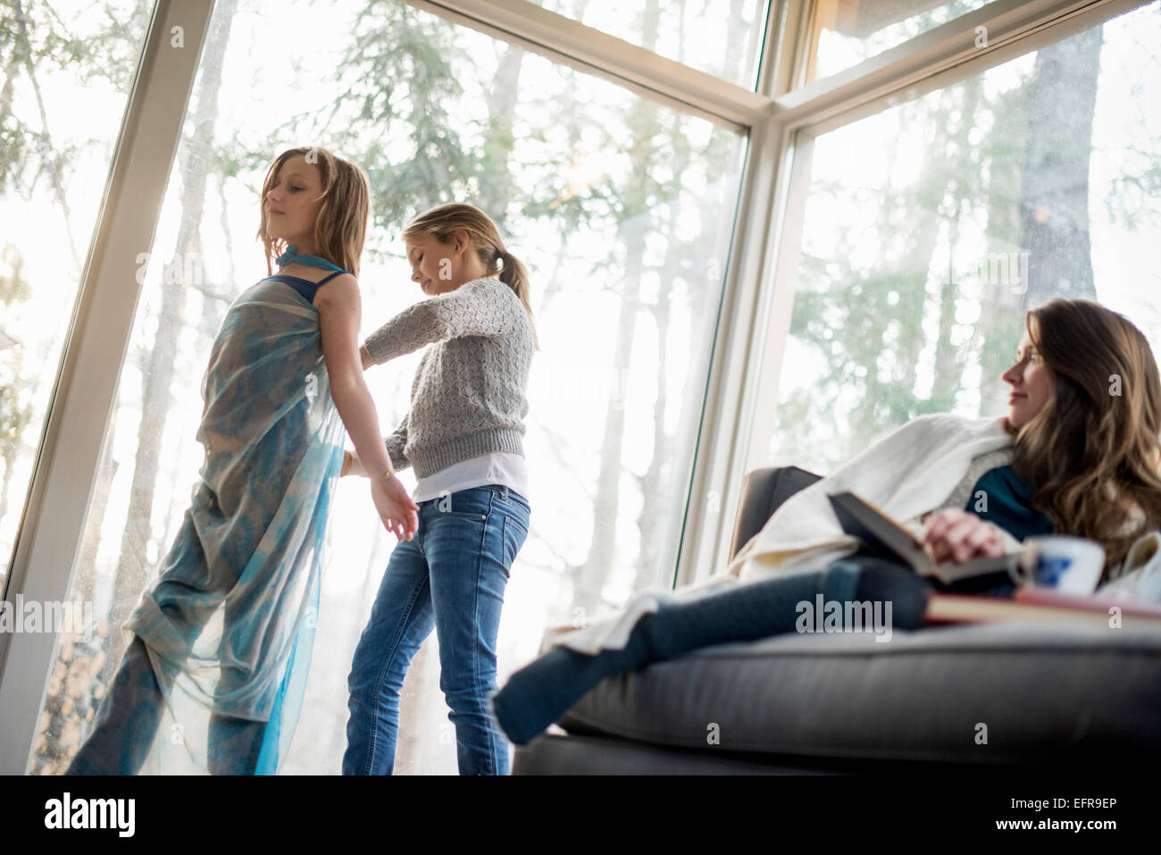 Zwei Mädchen stehen in einem Wohnzimmer, verkleiden, eine Frau auf einem Sofa sitzend beobachten. Stockfoto