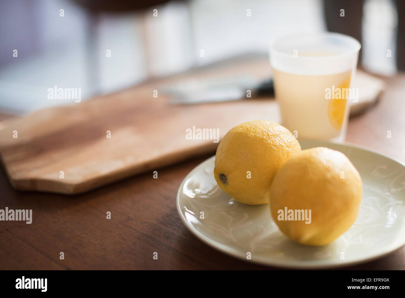 Ein Schneidebrett mit Messer, eine Platte mit zwei Zitronen und ein Glas auf einem Tisch. Stockfoto