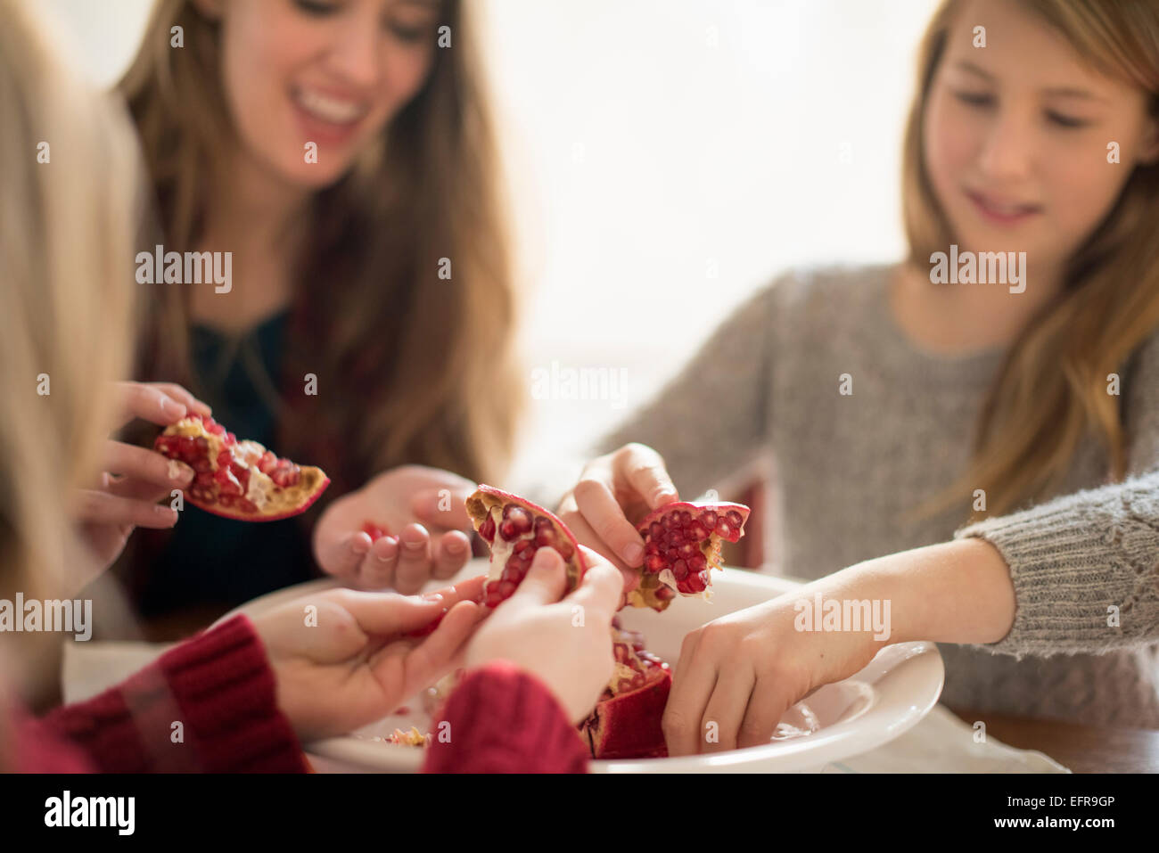 Zwei Mädchen und eine Frau sitzen an einem Tisch, Kommissionierung Kerne eines Granatapfels. Stockfoto