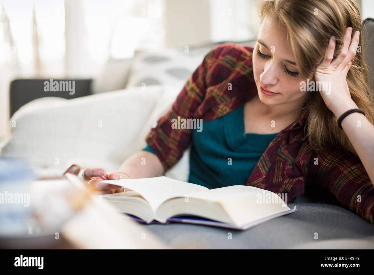Junge Frau sitzt auf einem Sofa, ein Buch zu lesen. Stockfoto