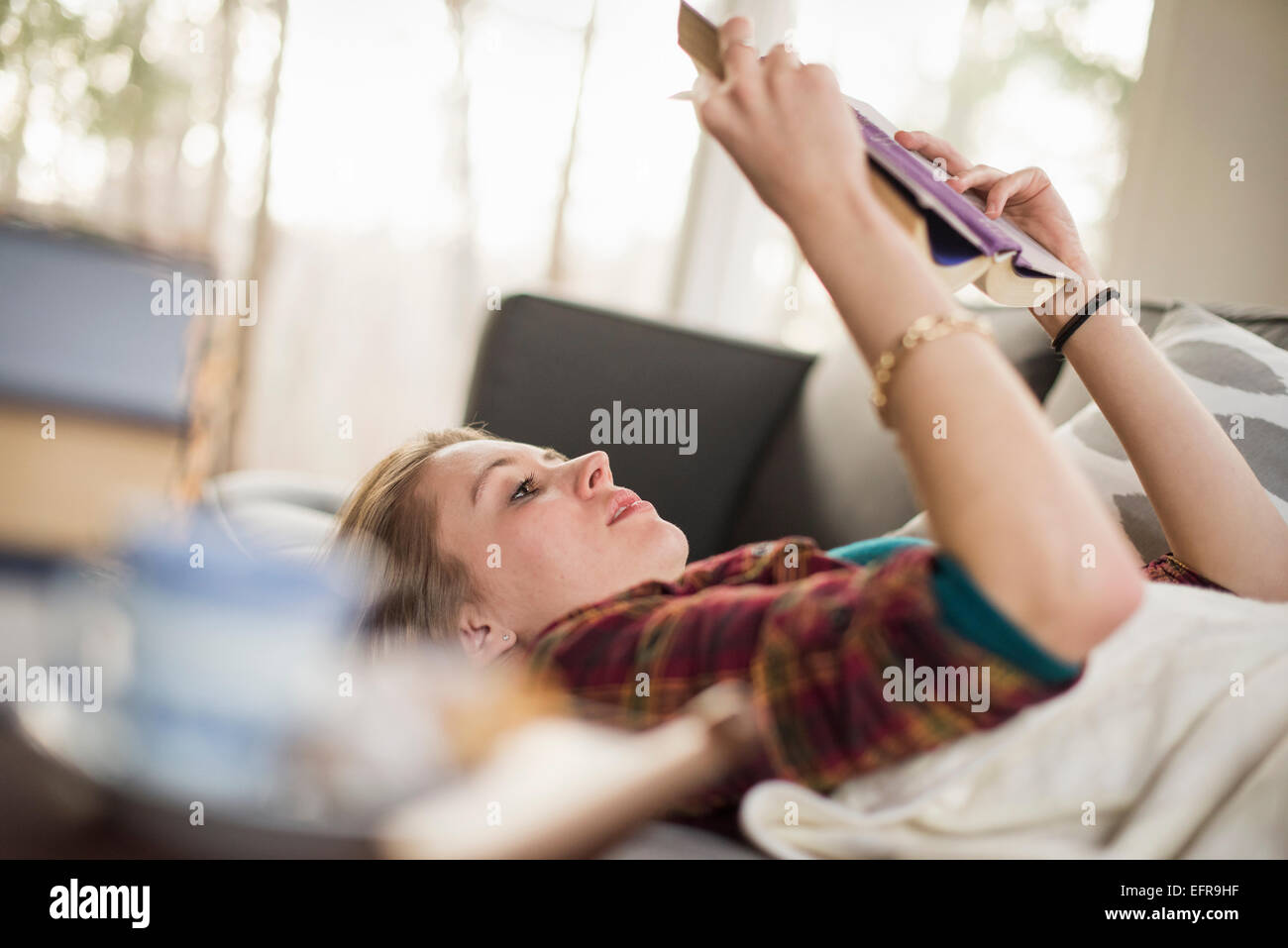 Junge Frau auf einem Sofa liegend ein Buch lesen. Stockfoto