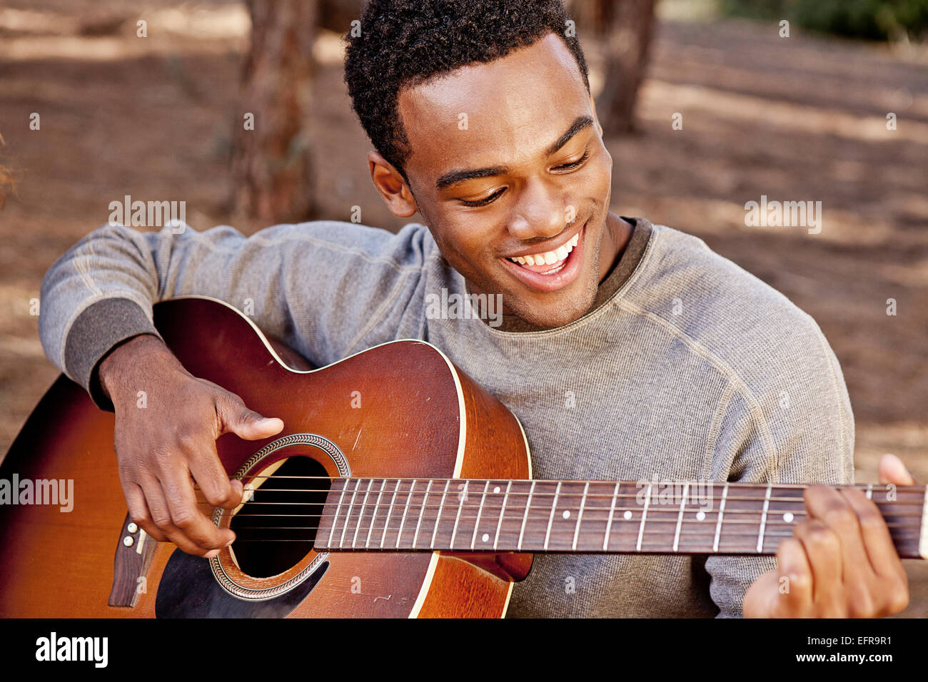Junger Mann sitzt im Wald spielt akustische Gitarre Stockfoto