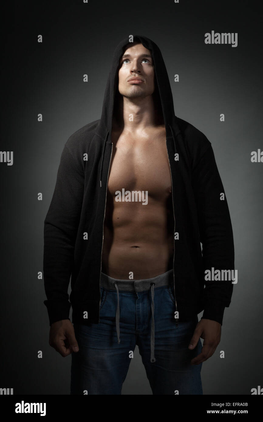 starker Mann mit schwarzer Hoodie isoliert auf dunklem Hintergrund Stockfoto