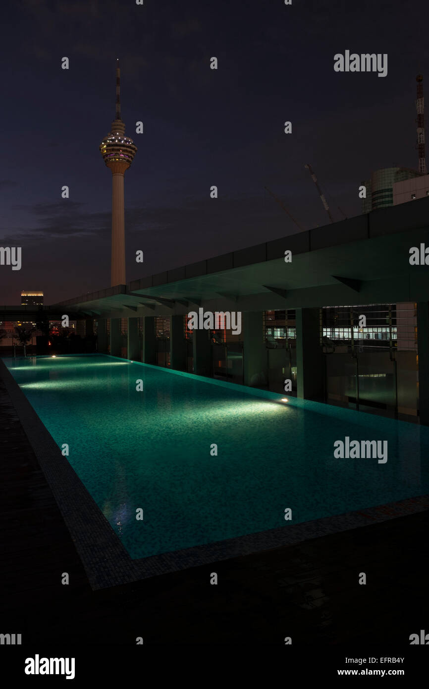 Der KL Tower, gesehen vom Dach eines nahe gelegenen Gebäudes in Kuala Lumpur, Malaysia, in der Nacht. Schwimmbad im Vordergrund. Stockfoto