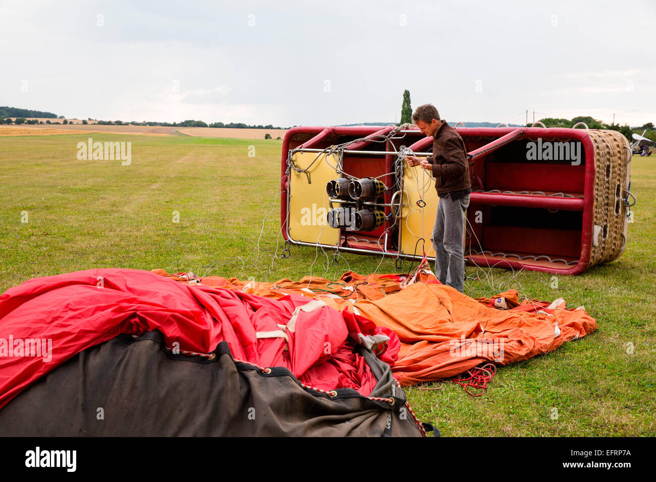 Mann, mit Seilen und Tauwerk für Heißluftballon Umschlag und Korb in Feld, South Oxfordshire, England Stockfoto