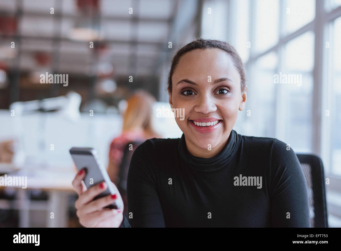 Porträt der fröhliche junge Frau mit einem Mobiltelefon. Afrikanerin, Blick auf die Kamera zu Lächeln bei der Arbeit. Stockfoto