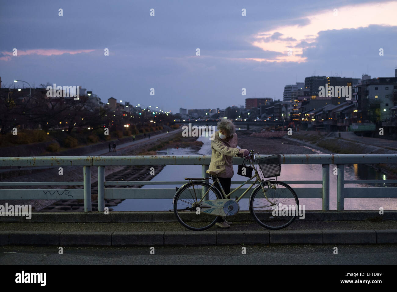 Ältere Frau trägt einen Mundschutz mit ihrem Fahrrad über den Fluss Kamogawa. Kyoto, Japan Stockfoto