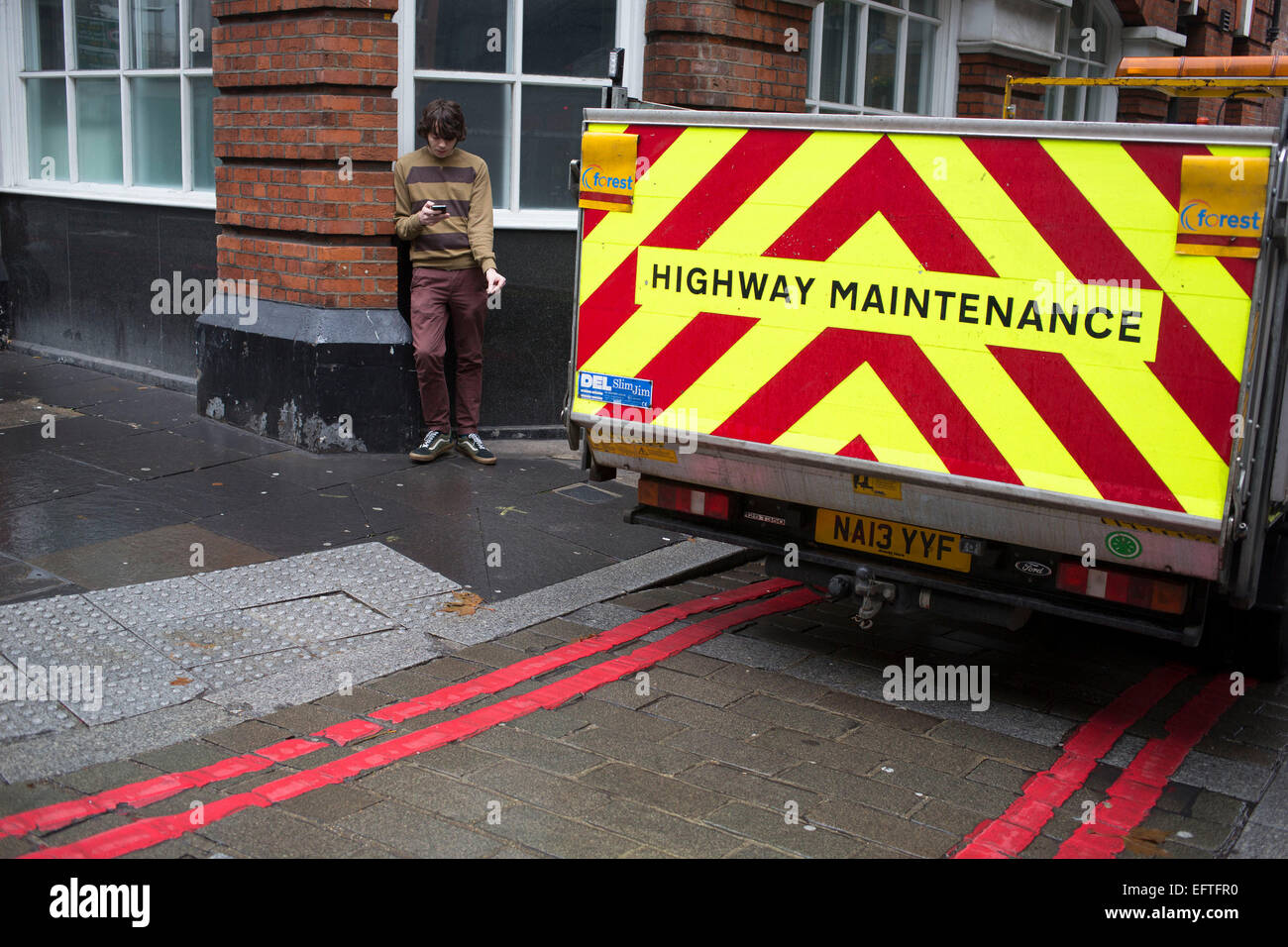 Autobahn Wartung Fahrzeug sieht aus wie es einige doppelten rote Linien mit Rädern, London, UK gelegt hat. In der Zwischenzeit ein junger Mann SMS während draußen haben eine Zigarettenpause. Stockfoto