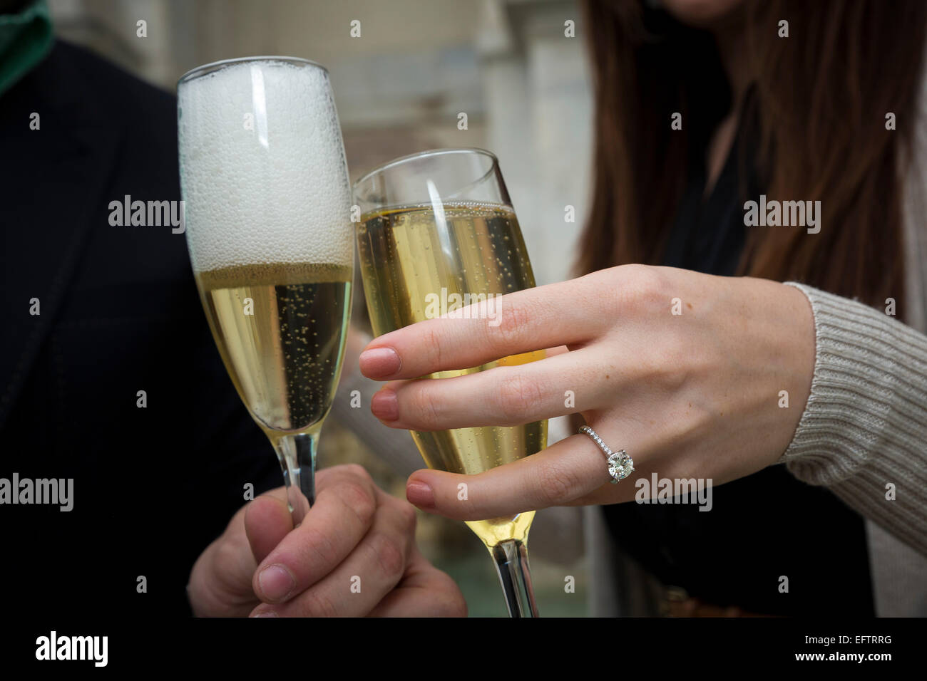 Verlobungsring auf Hand beim Anstoßen mit Sekt. Stockfoto