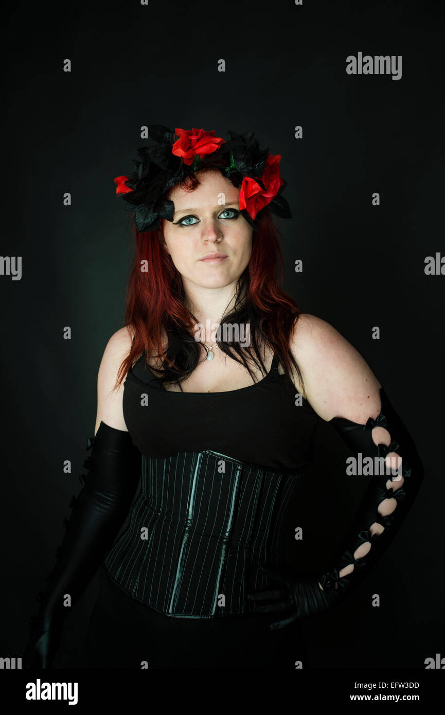 Eine junge rothaarige rote kurzhaarige Frau Goth Mädchen trägt ein schwarzes Korsett und langen schwarzen Ellenbogen-Handschuhe und roten Blumen im Haar Stockfoto