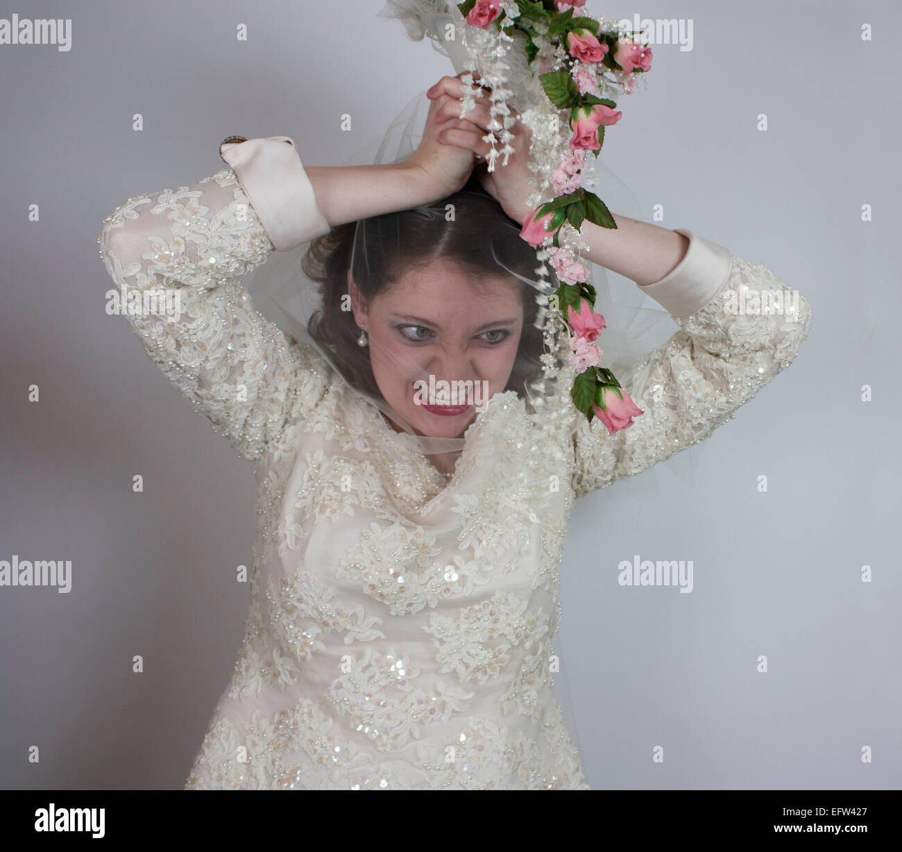 Hübsche junge Braut benimmt sich wie ein Bridezilla mit ihrem Blumenstrauß über Kopf und einen wahnsinnigen Blick auf ihrem Gesicht. Stockfoto