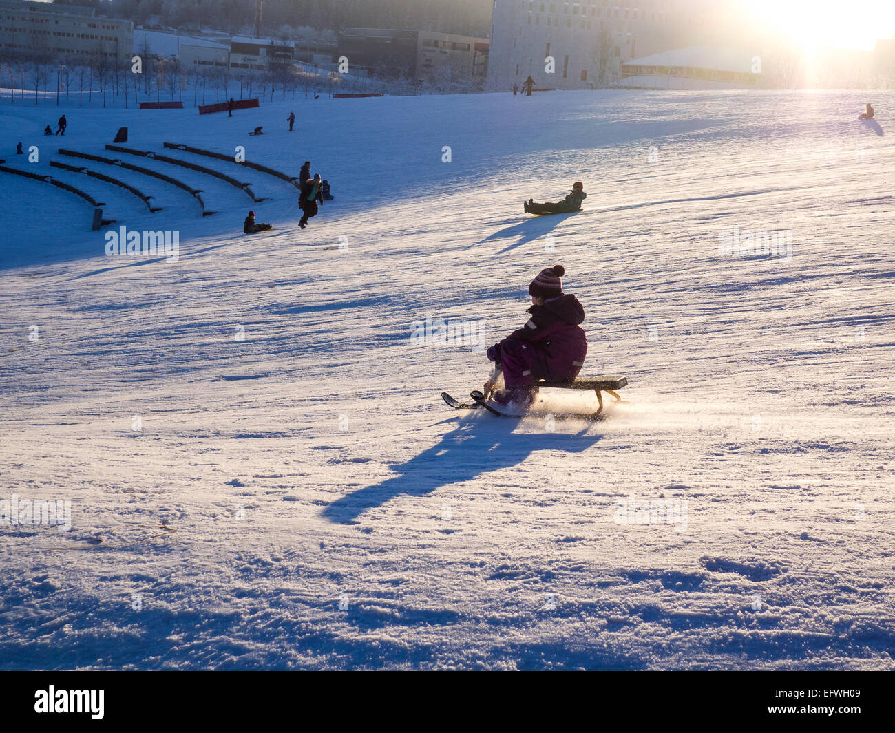 Kleiner Junge eine Rodelbahn einen verschneiten Hang hinunter in den Sonnenuntergang reiten Stockfoto