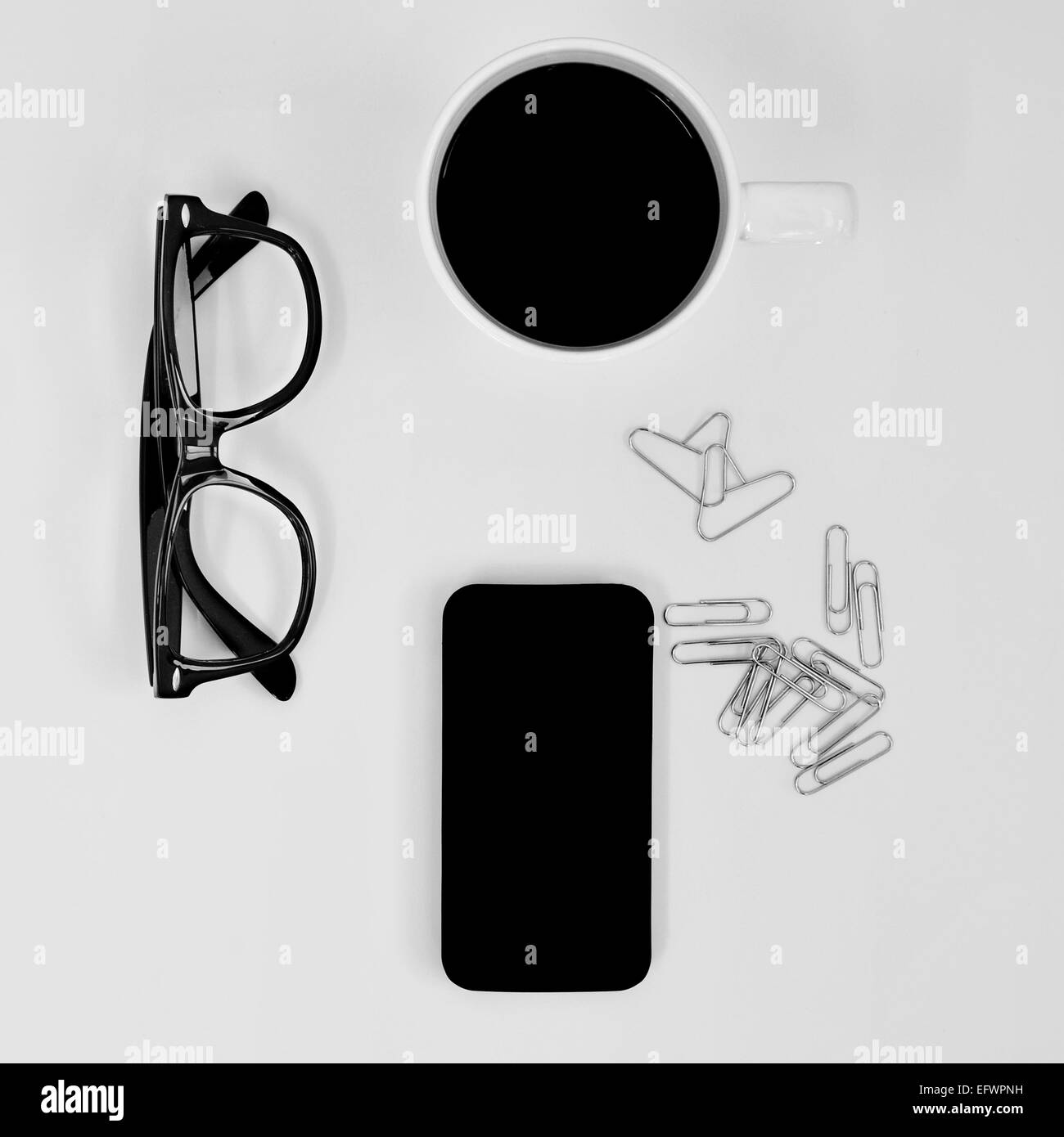 High-Angle Shot von ein paar Brillen, ein Smartphone, eine Tasse Kaffee und einige Büroklammern, zwei davon Herz-Shapped, auf ein Jota Stockfoto