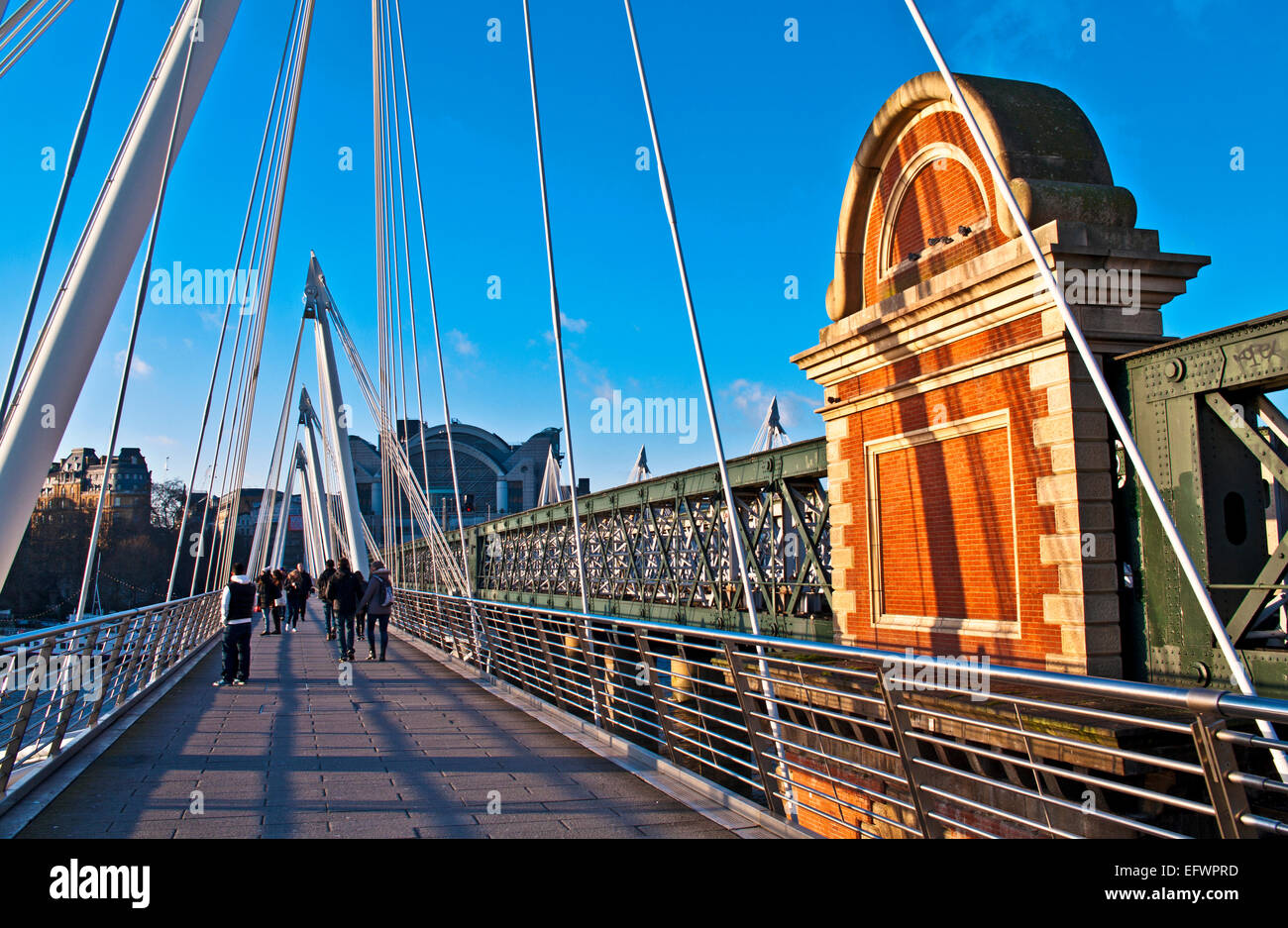 Touristen auf der Hungerford Bridge, central London, neben dem Bahnübergang Bahnhof Charing Cross im Hintergrund. Stockfoto