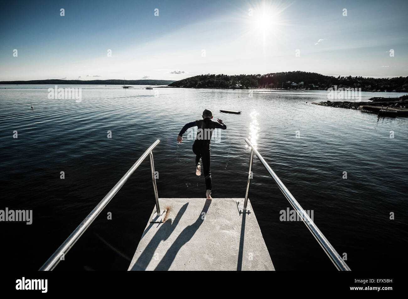 Ein Junge trägt einen Neoprenanzug Ulvøya in Oslo von einem Turm ins Wasser springen. Stockfoto