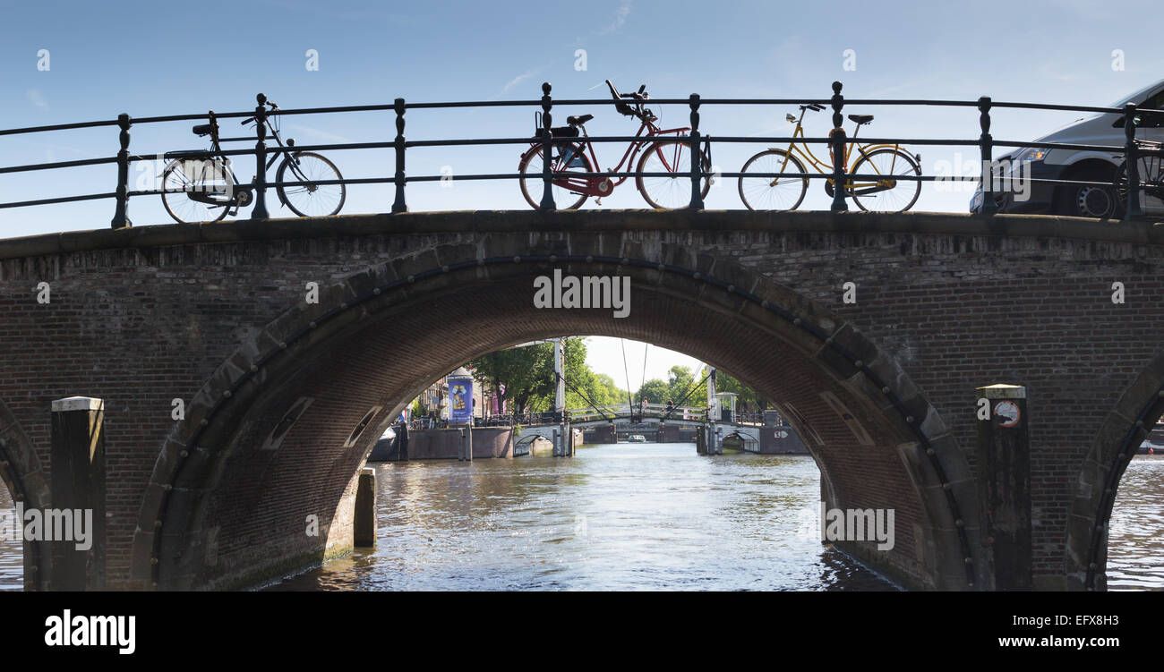 Fahrräder, angekettet an eine gewölbte Ziegelbrücke über einen Kanal in Amsterdam, Niederlande Stockfoto