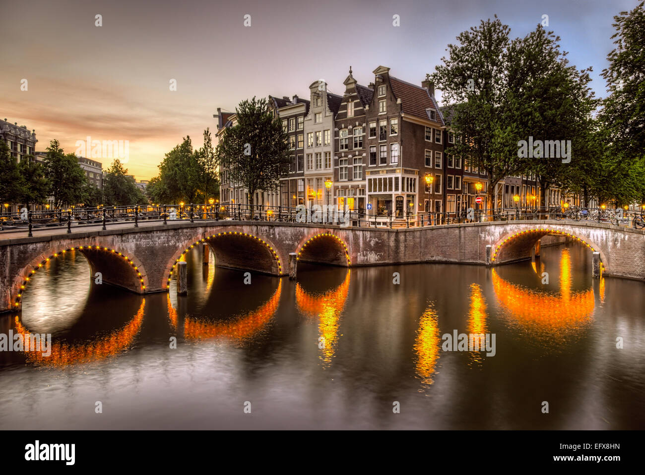 Beleuchtete Bogenbrücken gegossen leuchtende Reflexionen auf den Grachten in Amsterdam, Niederlande-Hervorhebung der markanten Architektur Stockfoto