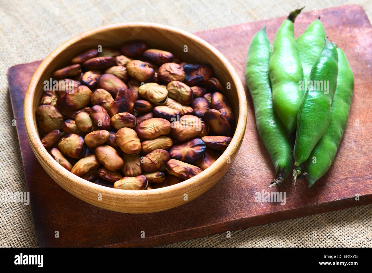 Geröstete Bohnen (lat. Vicia Faba) gegessen als Snack in Bolivien in Holzschale mit frischen Bohnen Schoten auf der Seite Stockfoto