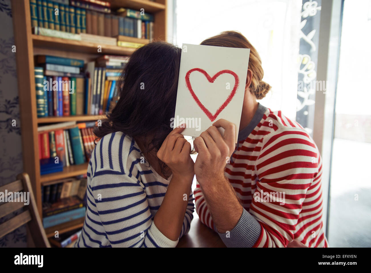 Flirty paar sitzt in Bibliothek hinter Papier mit roten Herzen Stockfoto
