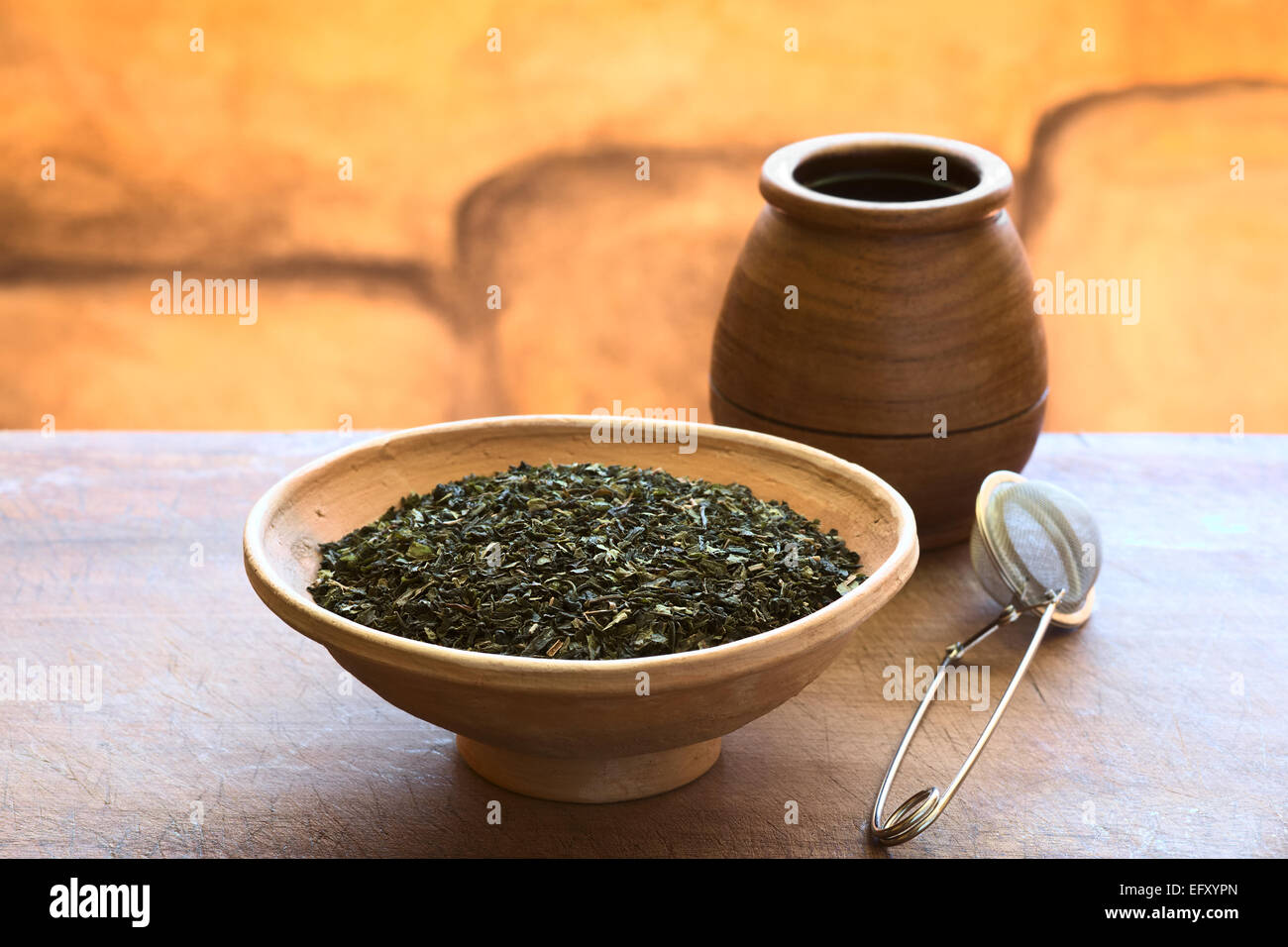 Getrocknete grüne Teeblätter in Schüssel mit einem Teesieb und hölzernen Teetasse mit Tageslicht fotografiert Stockfoto