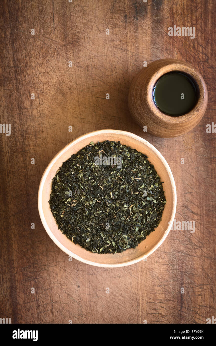Overhead Schuss getrockneter grüner Tee Blätter in Schüssel mit Tee in Holzbecher auf Holz mit Tageslicht fotografiert Stockfoto