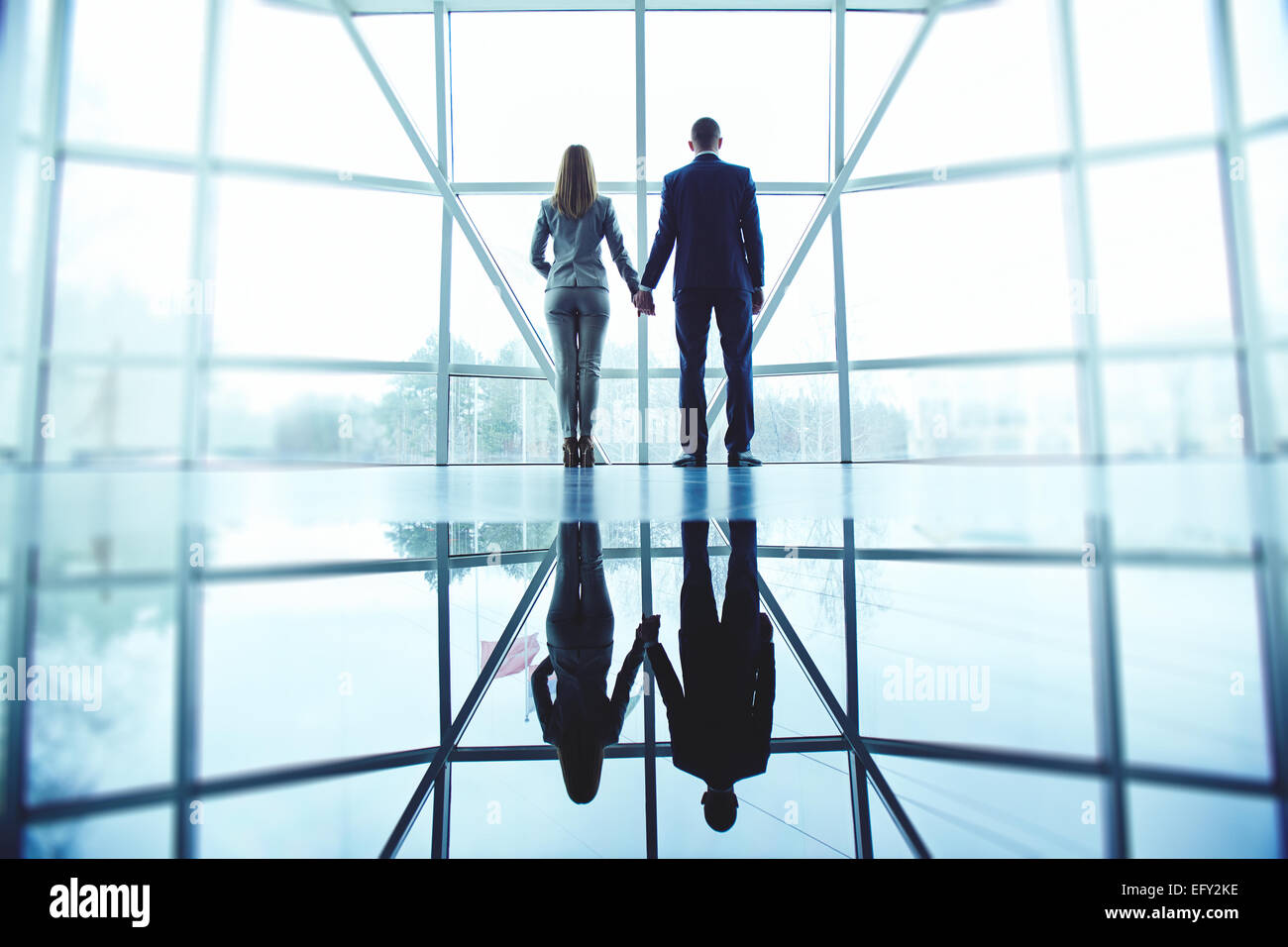 Junger Mann und Frau in festlich gekleidet, hält mit den Händen stehend durch Bürofenster Stockfoto
