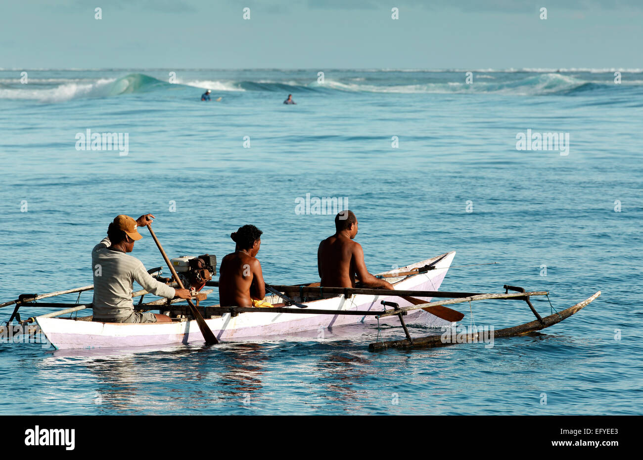 Fischer in hölzernen Ausleger-Kanu paddeln vorbei an Touristen Surfen in den Wellen in den Molukken, Indonesien Stockfoto