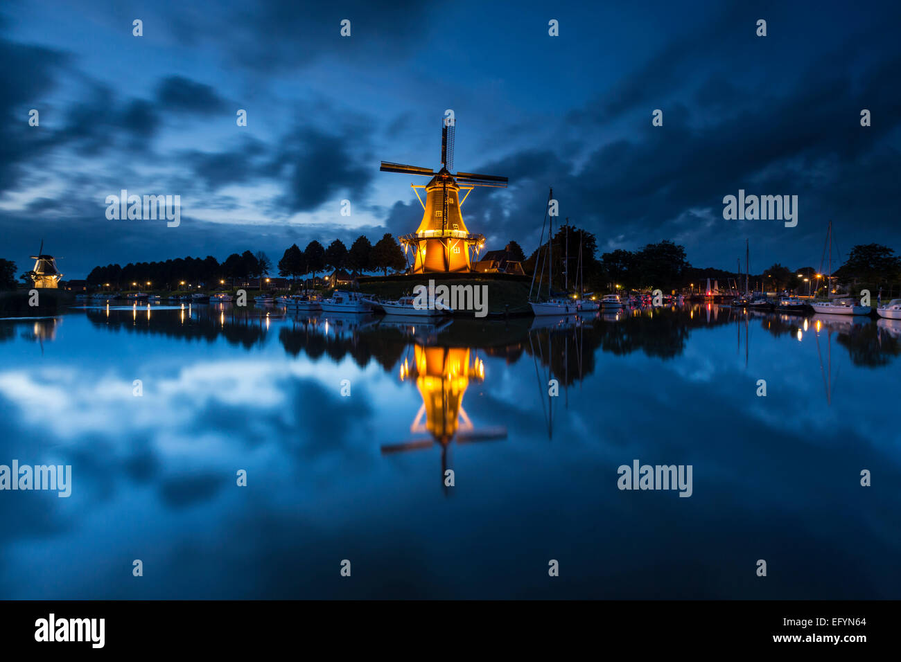 Windmühle in den Niederlanden in der Nacht mit Wolken und blauer Himmel im Hintergrund und Reflexionen über den Kanal Stockfoto