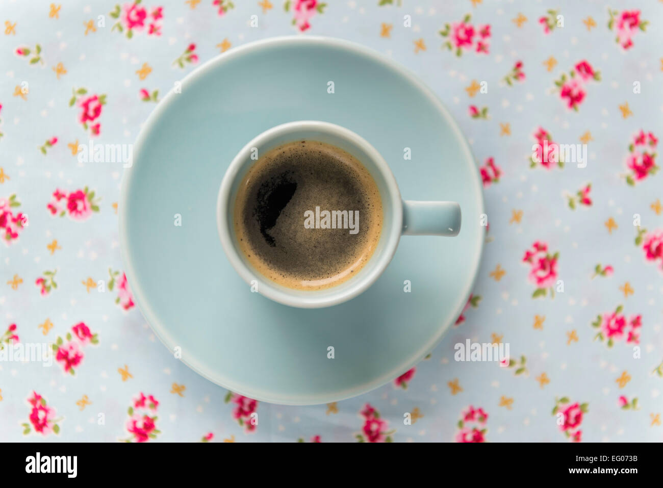 Espresso-Kaffeemaschine in einem blauen Tasse und Untertasse auf einer floral Tischdecke. Stockfoto