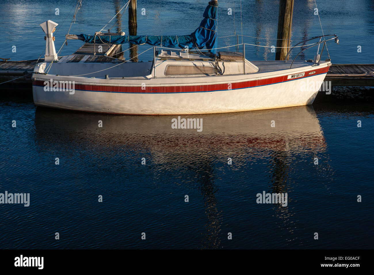 Gefleckte Reflexionen von einem kleinen Segelboot im Wasser, gefesselt an einen Zettel in einer Marina und für den Winter fest versiegelt. Stockfoto