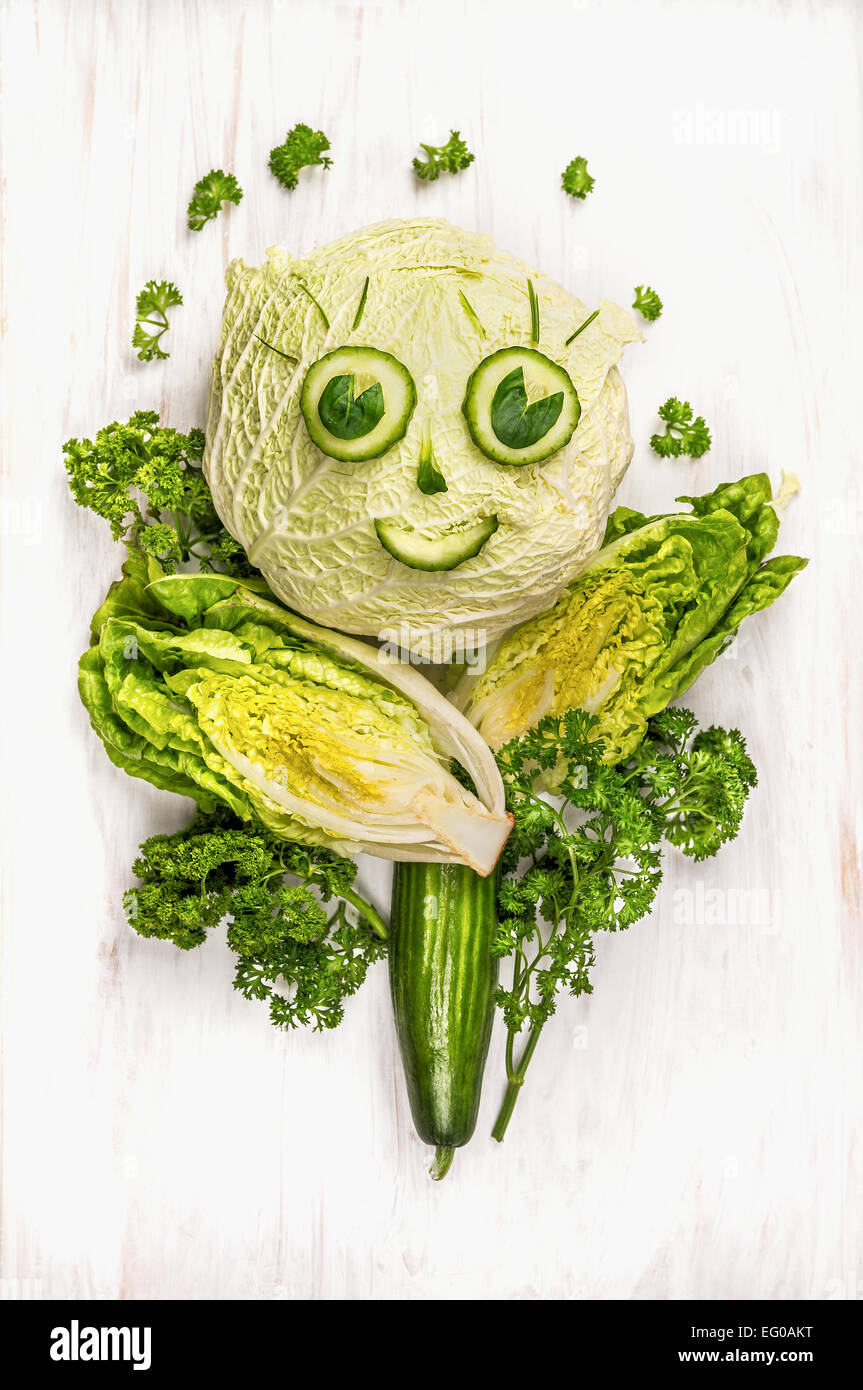 lustiges Mädchen Gesicht gemacht von grünem Gemüse, Gurken und Salat auf weißem Holz Hintergrund Stockfoto