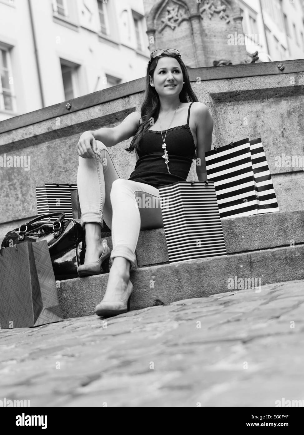 Foto von einer schönen jungen Frau sitzen und ausruhen mit ihren Einkaufstaschen in einen Brunnen in einer alten europäischen Stadt. Stockfoto