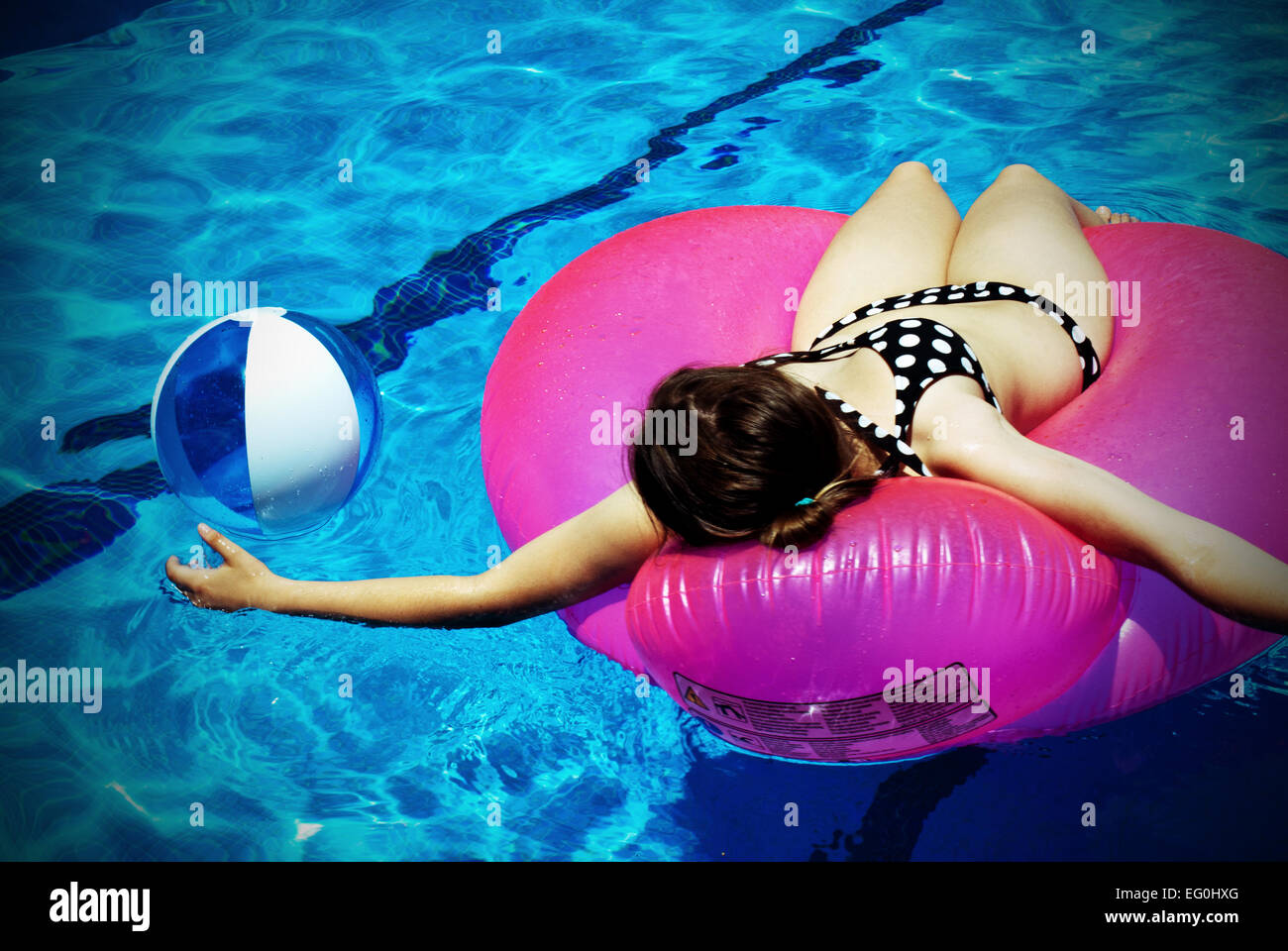 Frau auf einem aufblasbaren Gummiring liegend, die mit Ball in einem Schwimmbad spielt Stockfoto