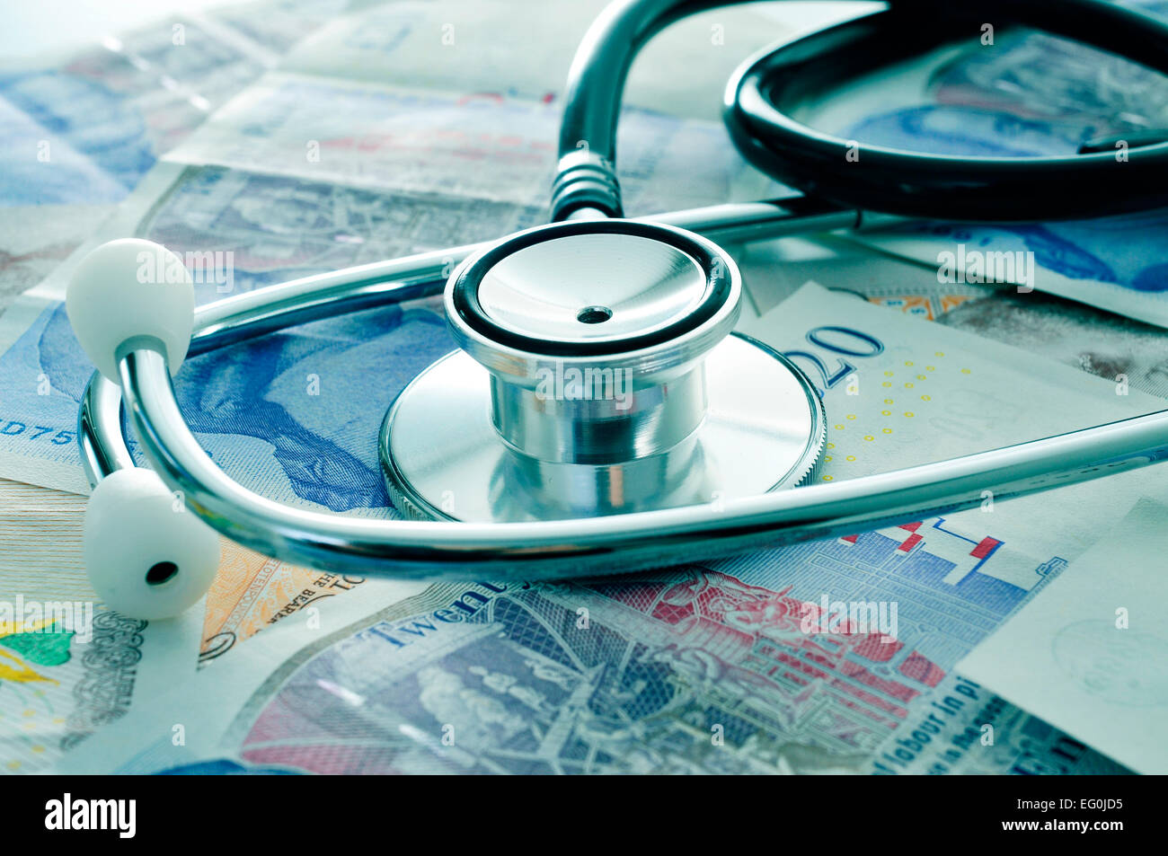 ein Stethoskop auf einen Haufen von Pfund Sterling Rechnungen, Darstellung der health care-Industrie-Konzept Stockfoto