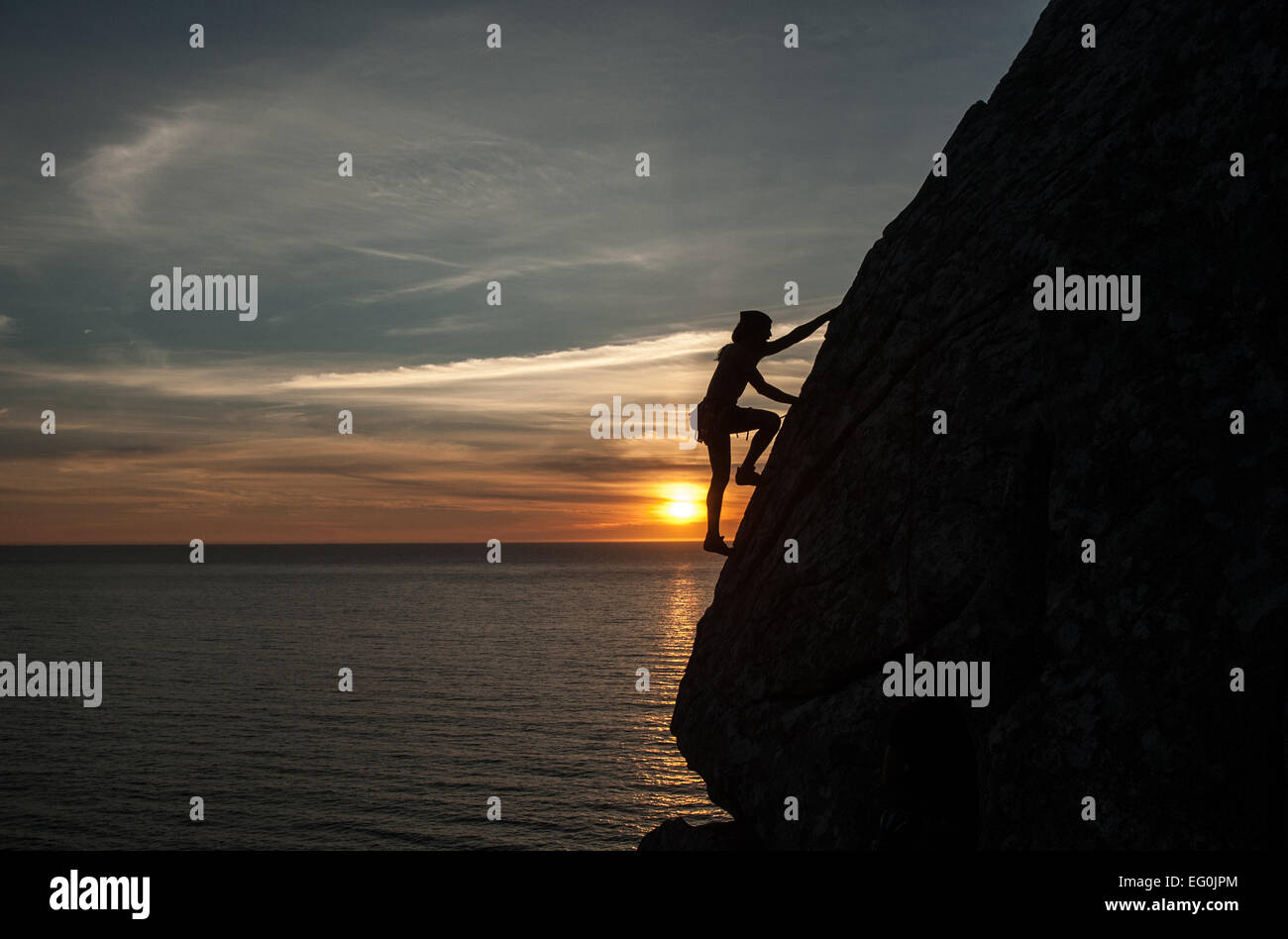 Silhouette der Frau Klettern Klippe bei Sonnenuntergang, Galicien, Spanien Stockfoto