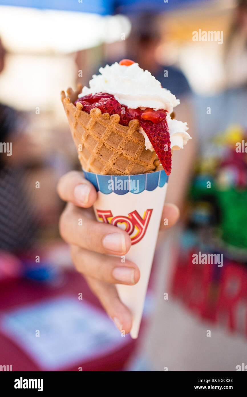 Frau Hand hält Eis-Kegel mit Erdbeeren und Sahne Stockfoto