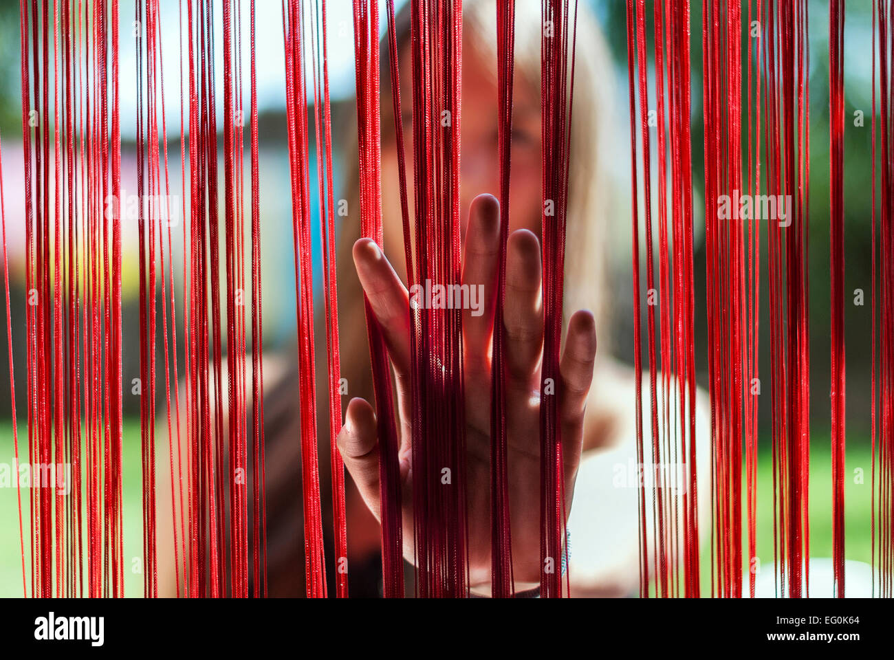 Frau, die ihre Hand durch einen Fransenvorhang legt Stockfoto