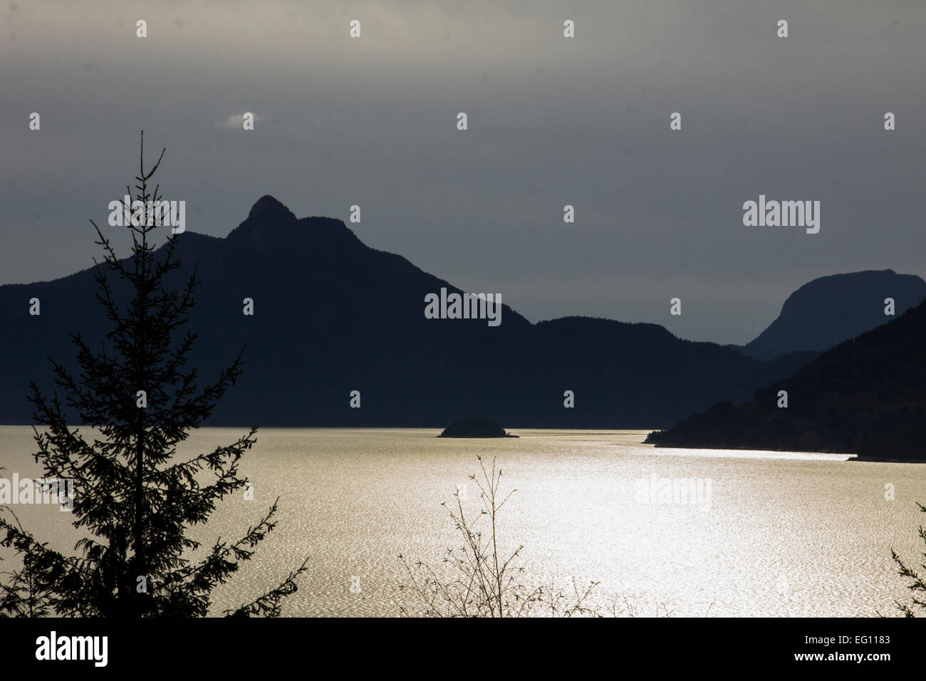 Berge, die Silhouette gegen den silbernen Wasser des Ozeans bei Sonnenuntergang. Stockfoto