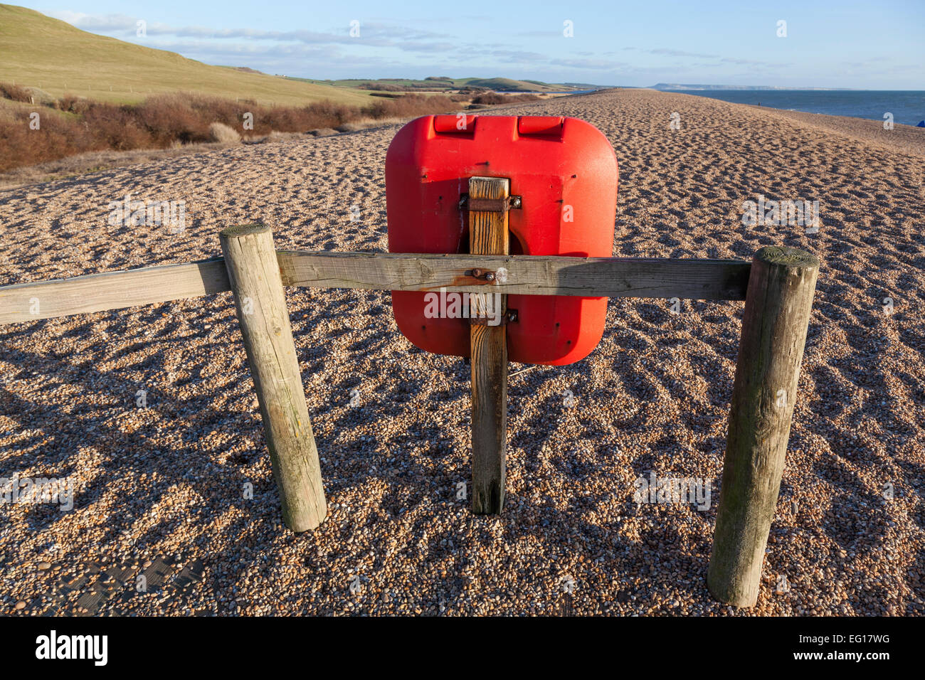 Orange/rot Kunststoff Rettungsring fest mit einem Holzzaun auf Chesil Beach Blick nach Osten in Richtung Portland Bill an einem Winter-Nachmittag. Stockfoto