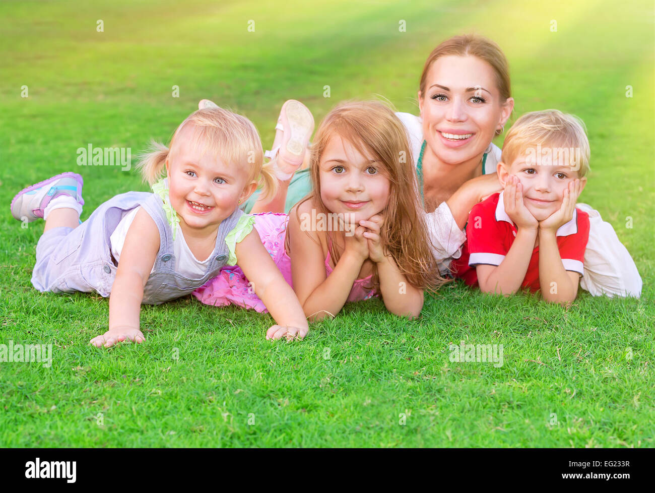 Glückliche große Familie Spaß im Freien, junge Mutter mit drei niedlichen Kinder liegend auf frischen grünen Wiese, Liebe und Zweisamkeit Stockfoto