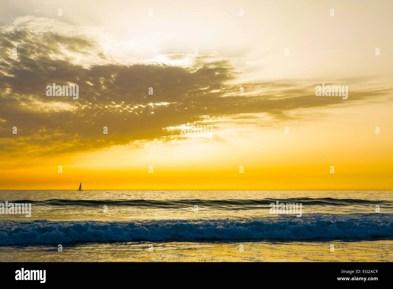 Sonnenuntergang an einem Strand in Andalusien, Spanien, mit einem Segelboot am Horizont Stockfoto