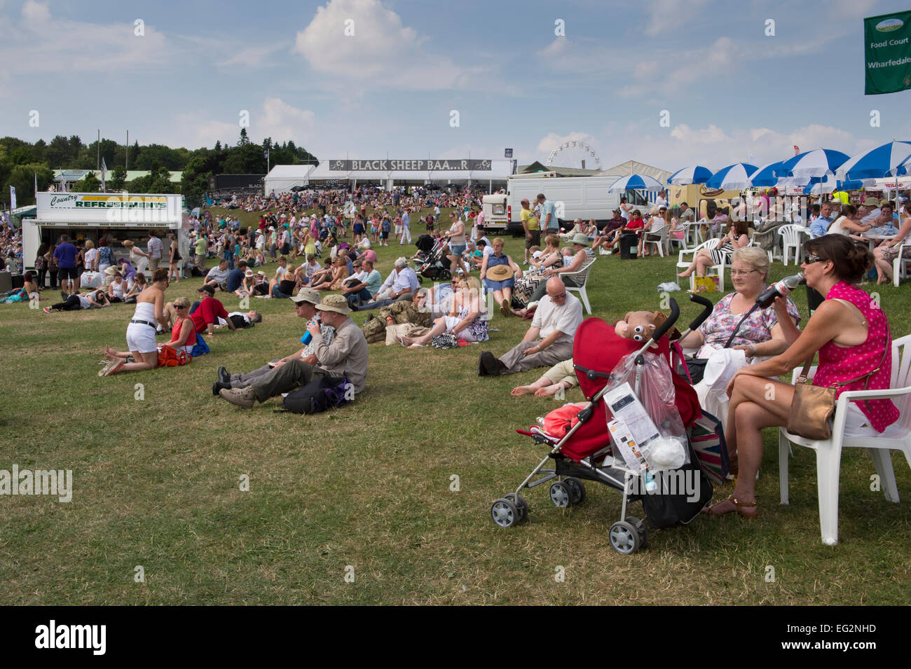 Tag für die Masse der Leute sitzen auf Gras oder Stühlen trinken, essen, Ruhen & Relaxen in der Sonne am großen Yorkshire, England, GB, UK. Stockfoto