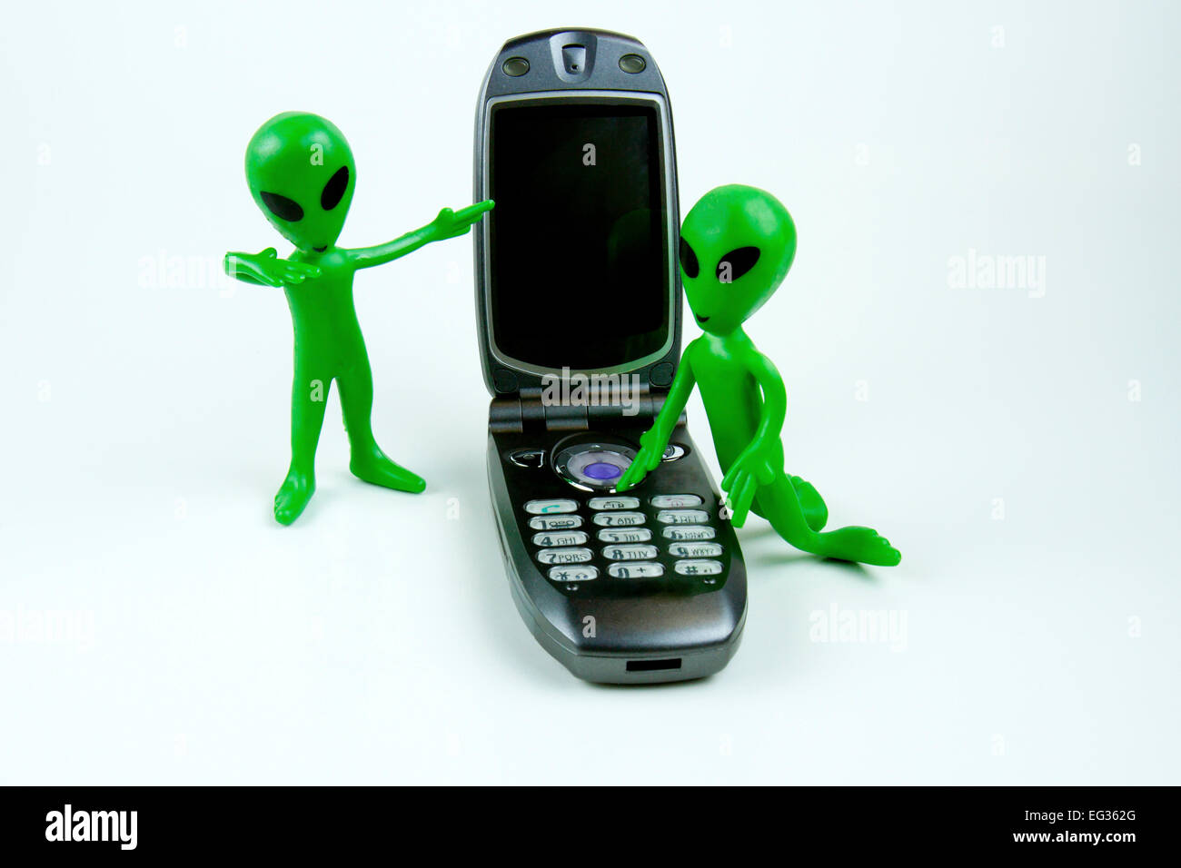 Kleinen grüner alien Mann anrufen mich Geste deutete auf ein Handy, während ein anderes Telefon wählt Stockfoto